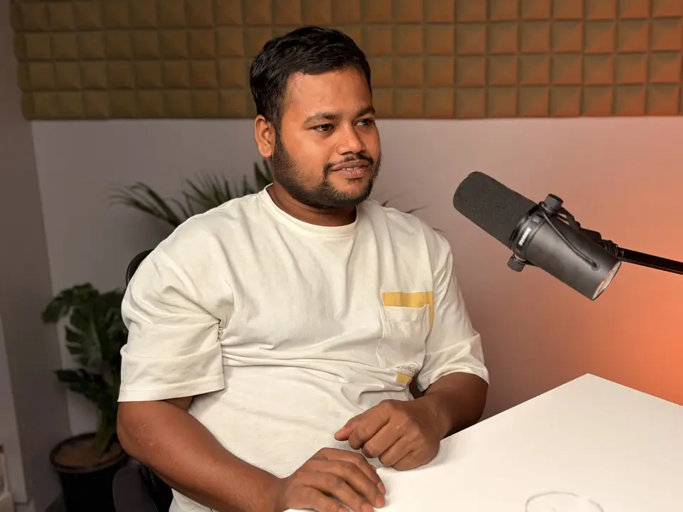 Guest seated at a desk beside a microphone, warm lamp behind