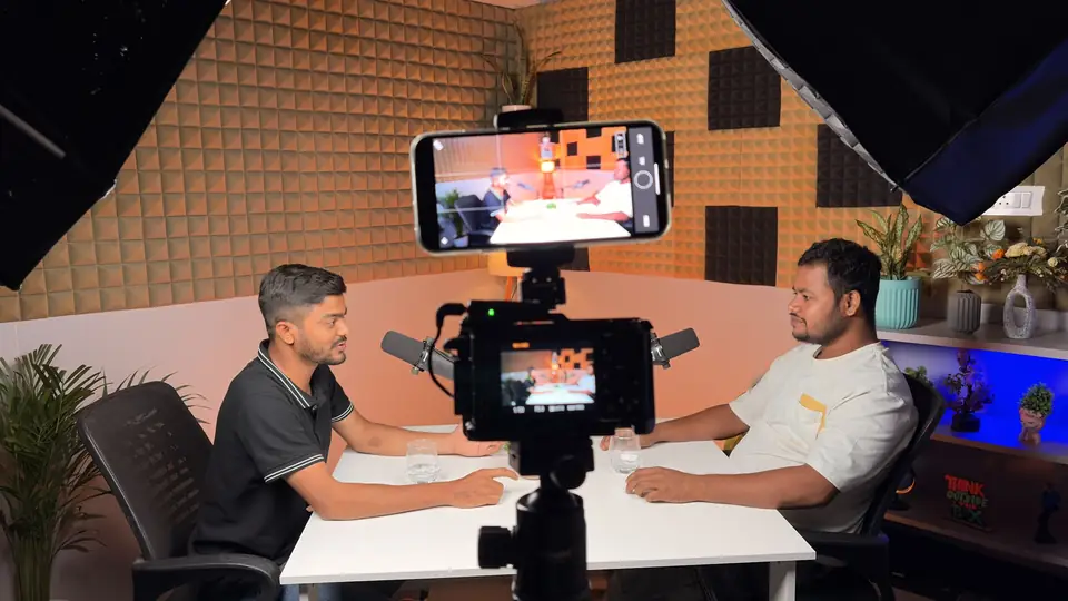 Two people recording a podcast on the acoustic-foam set with a phone monitor in front